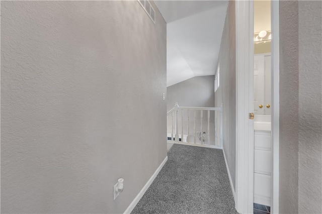 corridor featuring visible vents, baseboards, vaulted ceiling, carpet floors, and a textured wall