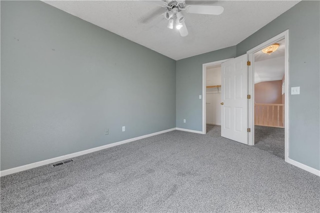 unfurnished bedroom featuring visible vents, a walk in closet, a textured ceiling, carpet floors, and baseboards