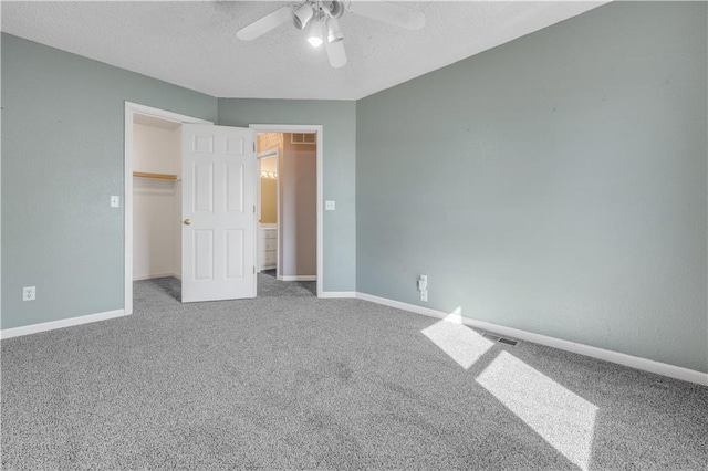 unfurnished bedroom with a walk in closet, baseboards, a textured ceiling, and carpet flooring