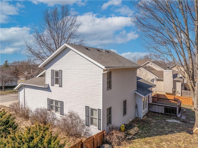 view of side of home featuring fence and a shingled roof