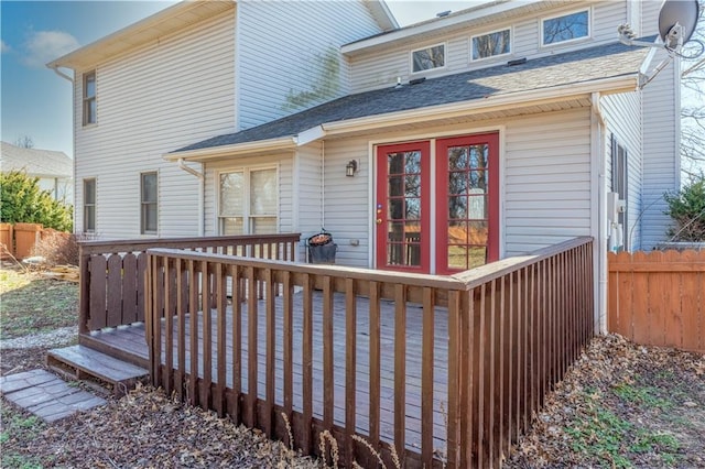 entrance to property with a deck, fence, and roof with shingles