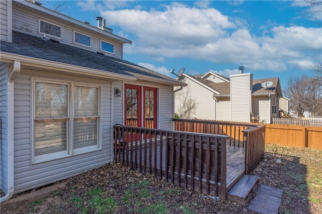 entrance to property with a wooden deck, roof with shingles, and fence