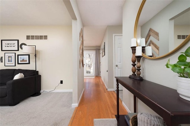 hall with visible vents, baseboards, and wood finished floors