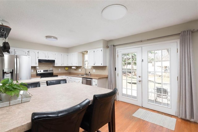 kitchen with white cabinets, stainless steel appliances, light wood-type flooring, and a sink