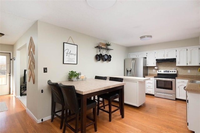 kitchen featuring light wood-type flooring, under cabinet range hood, tasteful backsplash, white cabinetry, and appliances with stainless steel finishes