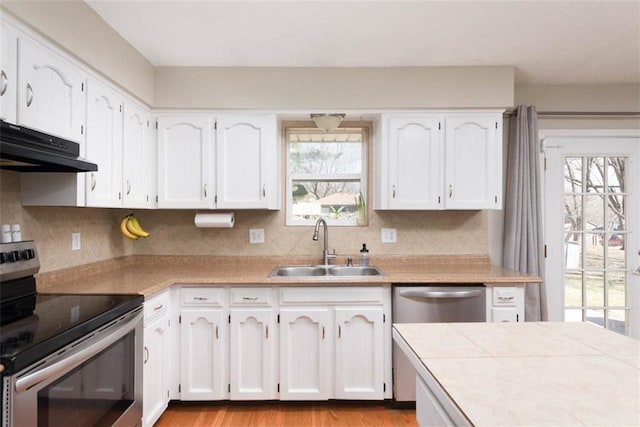 kitchen with under cabinet range hood, appliances with stainless steel finishes, white cabinetry, and a sink