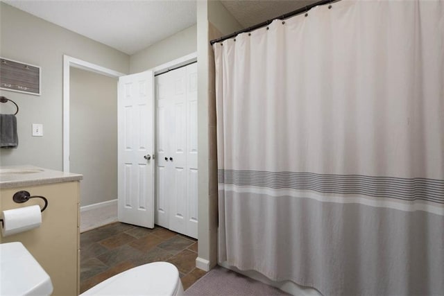 full bath with toilet, stone finish flooring, curtained shower, baseboards, and vanity