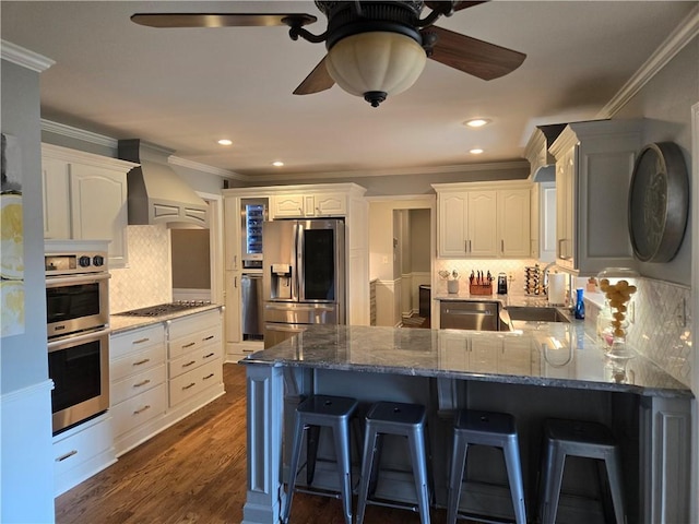 kitchen featuring dark wood finished floors, appliances with stainless steel finishes, a peninsula, custom exhaust hood, and a ceiling fan