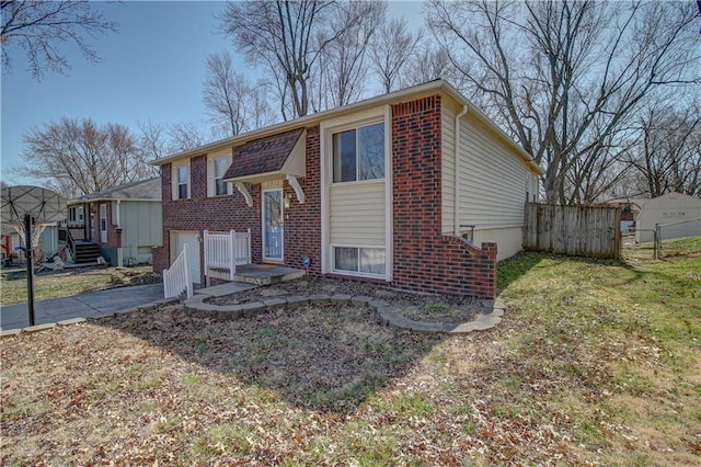 bi-level home featuring brick siding, an attached garage, a front lawn, fence, and driveway