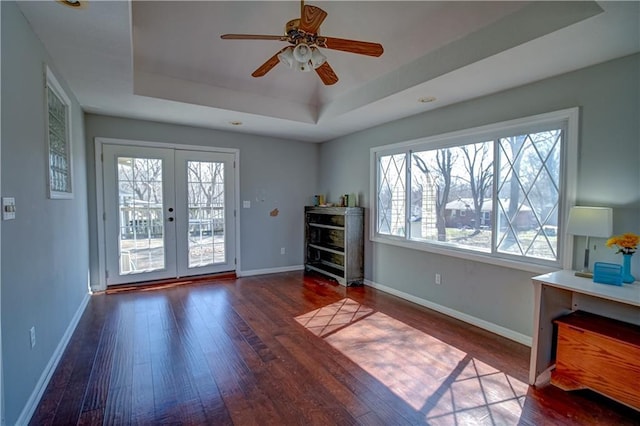 interior space with baseboards, a raised ceiling, wood finished floors, and a ceiling fan