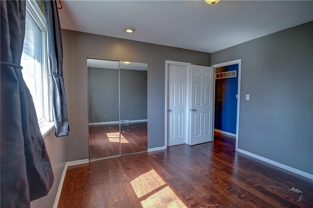 unfurnished bedroom with two closets, baseboards, and wood finished floors