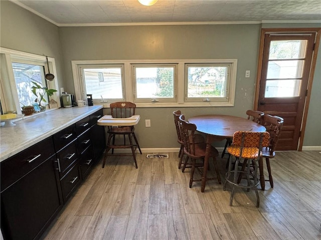 dining space with plenty of natural light, crown molding, and light wood finished floors