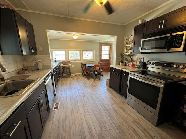 kitchen featuring a sink, ornamental molding, light wood-type flooring, and stainless steel appliances