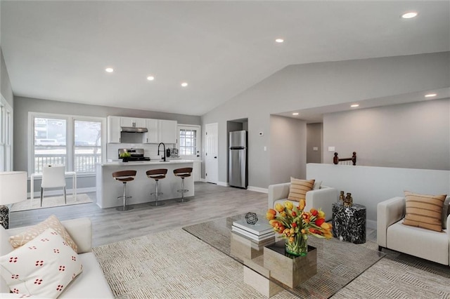 living room featuring vaulted ceiling, recessed lighting, baseboards, and light wood finished floors