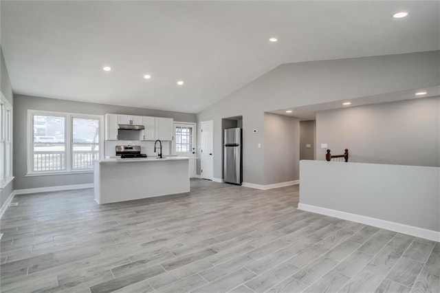 unfurnished living room with vaulted ceiling, baseboards, light wood-style floors, and a sink