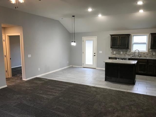 kitchen featuring backsplash, a center island, vaulted ceiling, light carpet, and a sink