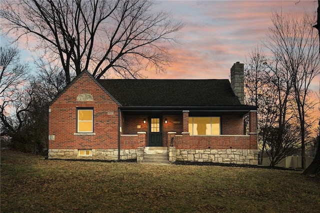 view of front of home with brick siding, a chimney, and a front yard