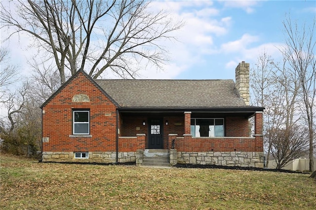 view of front of property featuring brick siding, a chimney, a front lawn, and roof with shingles