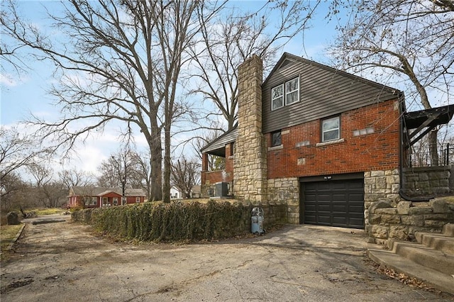 view of side of home featuring aphalt driveway, an attached garage, stone siding, and a chimney