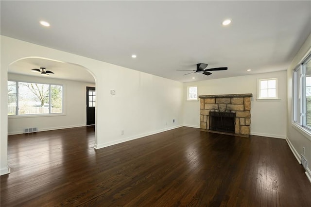 unfurnished living room with dark wood-style floors, a ceiling fan, visible vents, and arched walkways