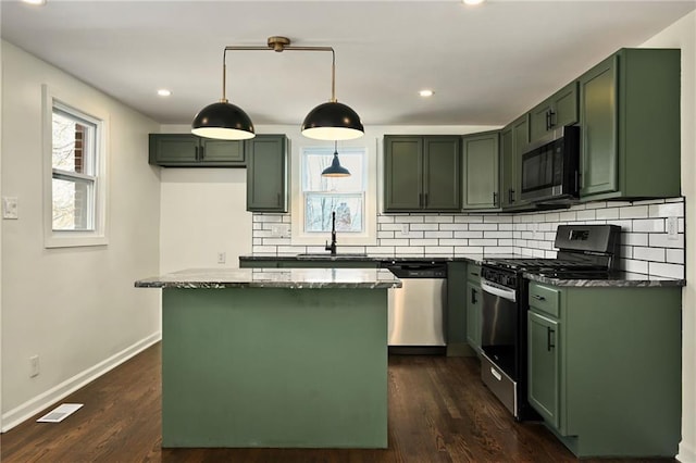 kitchen featuring dark stone countertops, a kitchen island, green cabinetry, a sink, and stainless steel appliances