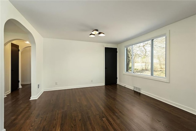 spare room featuring dark wood finished floors, baseboards, visible vents, and arched walkways