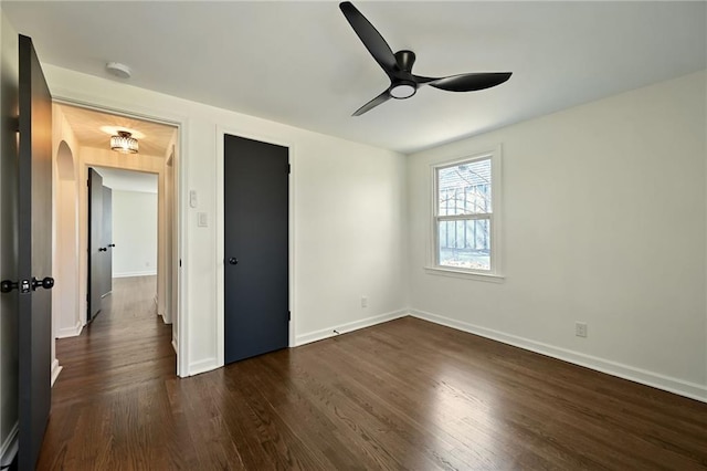 unfurnished bedroom with arched walkways, a ceiling fan, baseboards, and dark wood-style flooring