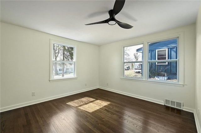 spare room featuring dark wood-type flooring, a ceiling fan, visible vents, and baseboards