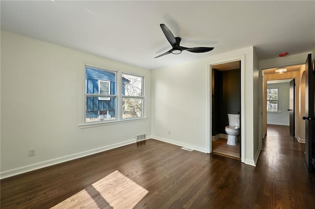 unfurnished bedroom featuring a ceiling fan, dark wood-style floors, baseboards, visible vents, and ensuite bath