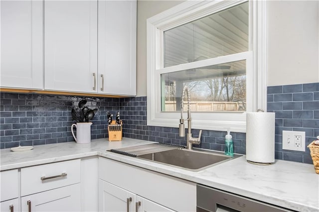 kitchen with a sink, light stone countertops, dishwasher, and white cabinets