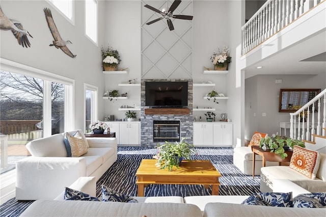 living room featuring a towering ceiling, a large fireplace, ceiling fan, and stairway