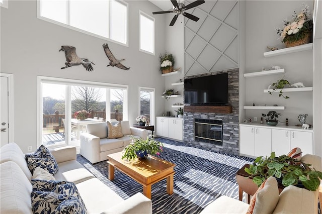 living room with a fireplace, ceiling fan, a healthy amount of sunlight, and a high ceiling