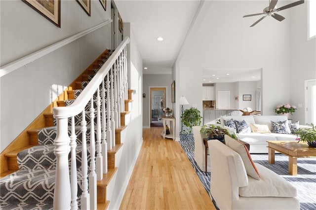 living room with light wood-style flooring, stairway, ceiling fan, recessed lighting, and a high ceiling
