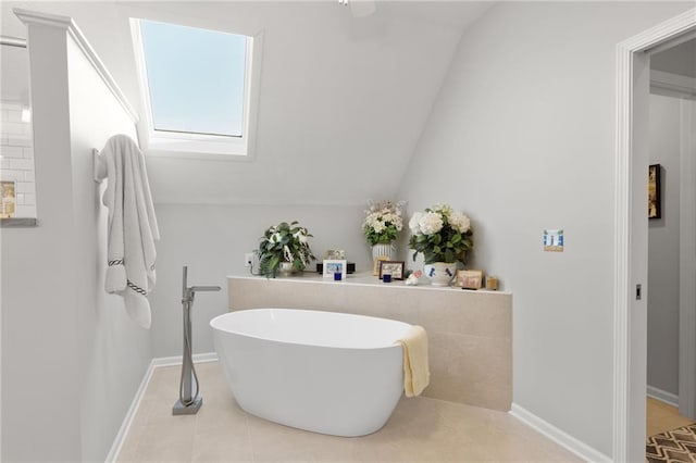 full bathroom featuring a soaking tub, vaulted ceiling with skylight, tile patterned flooring, and baseboards