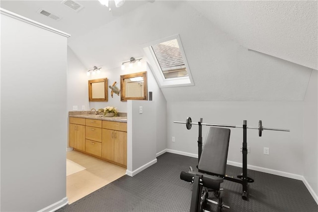 exercise area featuring baseboards, visible vents, ceiling fan, and vaulted ceiling with skylight