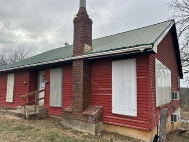 back of property featuring metal roof, cooling unit, and a chimney