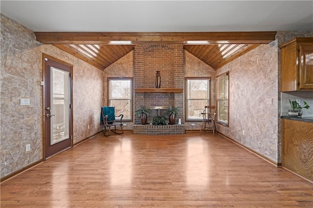 unfurnished living room with lofted ceiling with beams, a brick fireplace, wood finished floors, and wooden ceiling