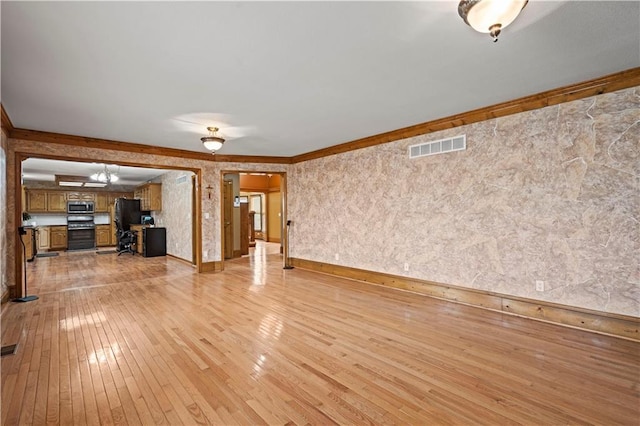 unfurnished living room featuring visible vents, baseboards, ornamental molding, and light wood finished floors