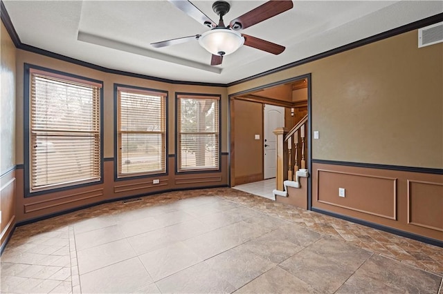 spare room with visible vents, a tray ceiling, ornamental molding, a decorative wall, and a ceiling fan