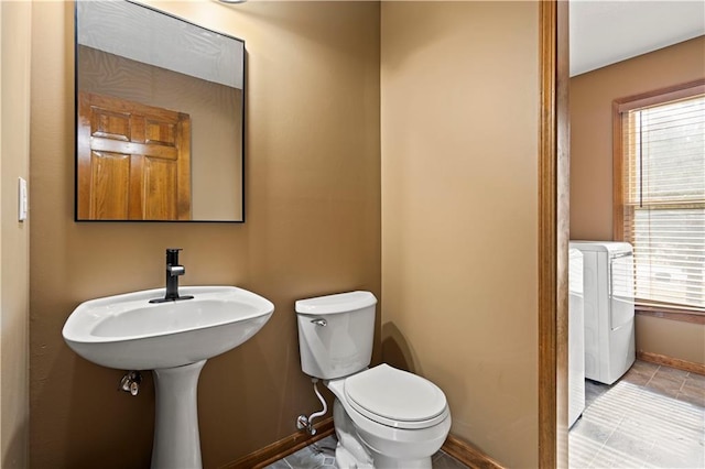 half bathroom with toilet, baseboards, and separate washer and dryer