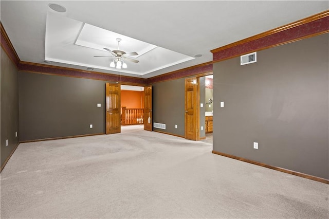 carpeted spare room with a tray ceiling, baseboards, visible vents, and a ceiling fan