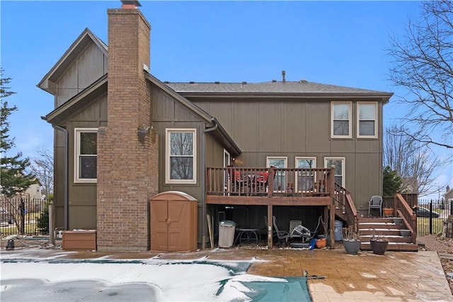 snow covered house with a wooden deck, a chimney, stairs, and fence