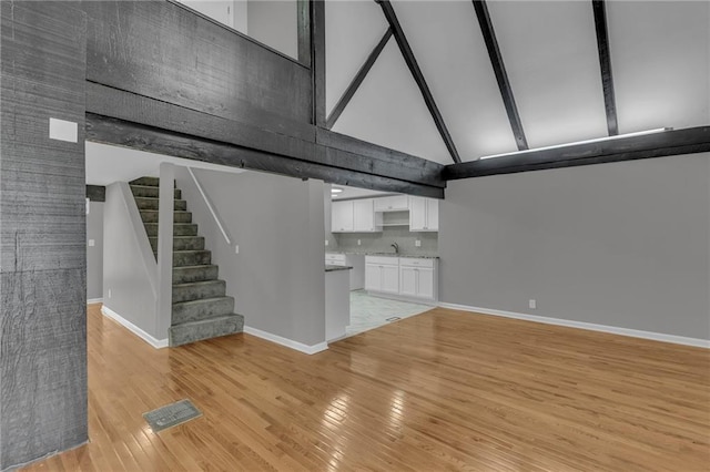 unfurnished living room featuring visible vents, baseboards, beam ceiling, light wood-style flooring, and high vaulted ceiling