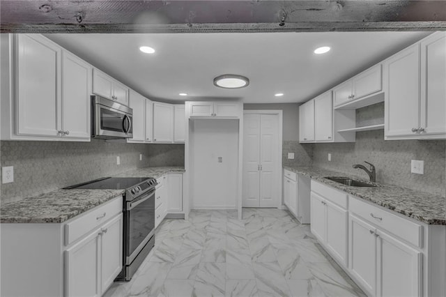 kitchen with light stone counters, appliances with stainless steel finishes, white cabinets, marble finish floor, and a sink