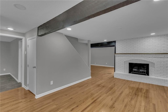 finished below grade area featuring a brick fireplace, baseboards, and wood finished floors