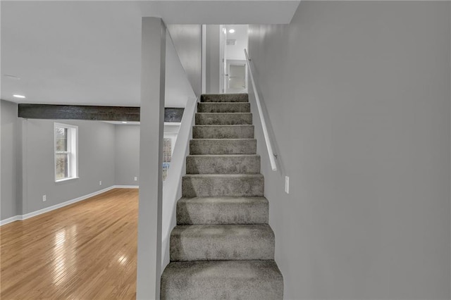 staircase featuring beam ceiling, baseboards, and wood-type flooring