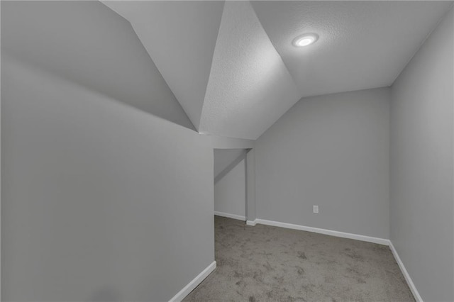 interior space with vaulted ceiling, carpet, baseboards, and a textured ceiling