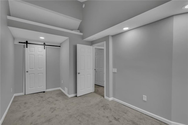 unfurnished bedroom featuring visible vents, baseboards, a barn door, and carpet floors