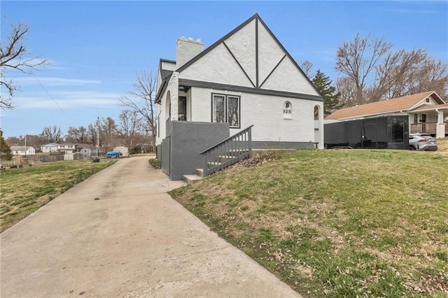 view of home's exterior featuring brick siding, a chimney, concrete driveway, and a lawn