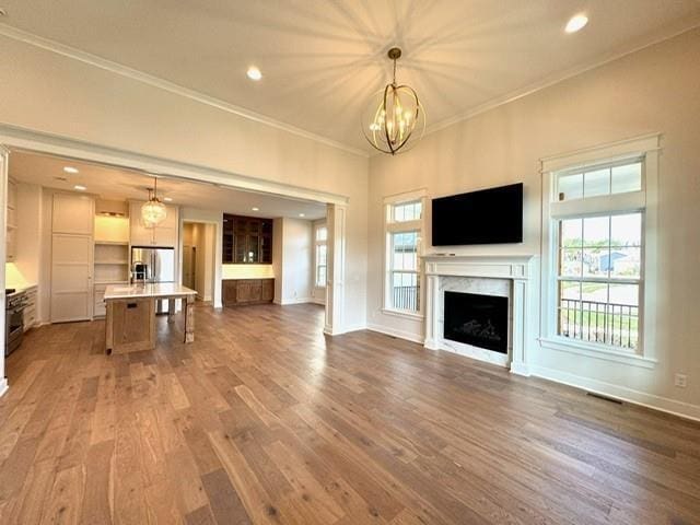 unfurnished living room featuring wood finished floors, baseboards, a fireplace, crown molding, and a notable chandelier